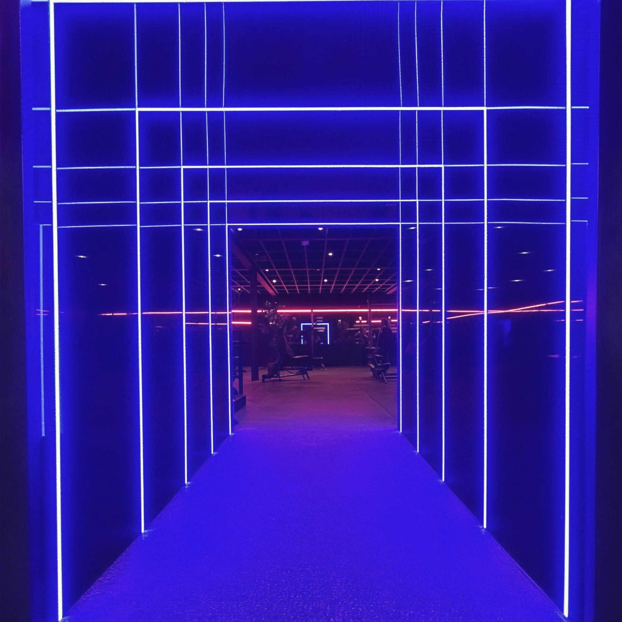 Perfectly symmetrical electric-blue LED grid tunnel with a glowing blue walkway leading into the gym floor.