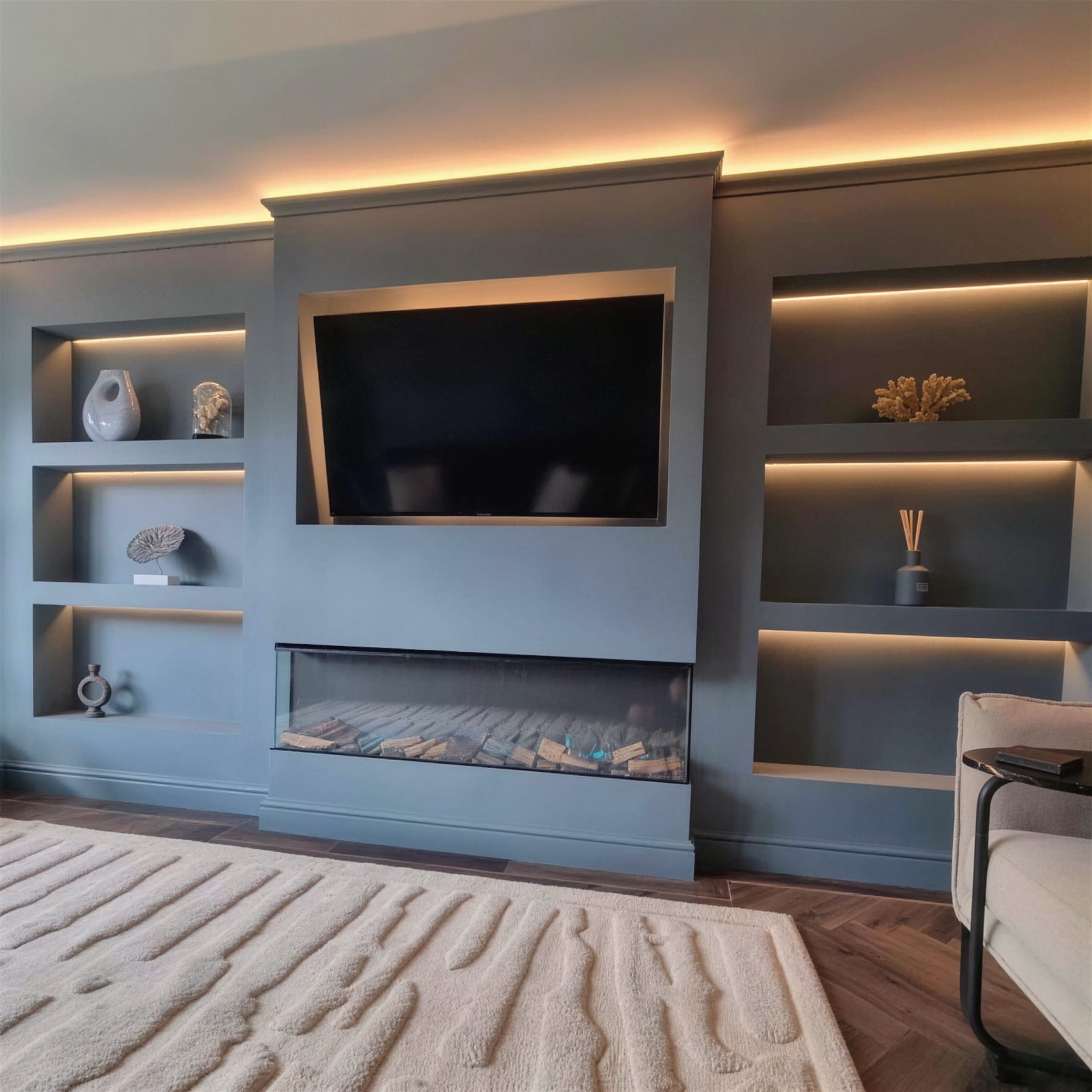 Fully styled blue-grey media wall: warm LED coves over shelving niches, linear fire glowing beneath the TV, textured rug in the foreground.