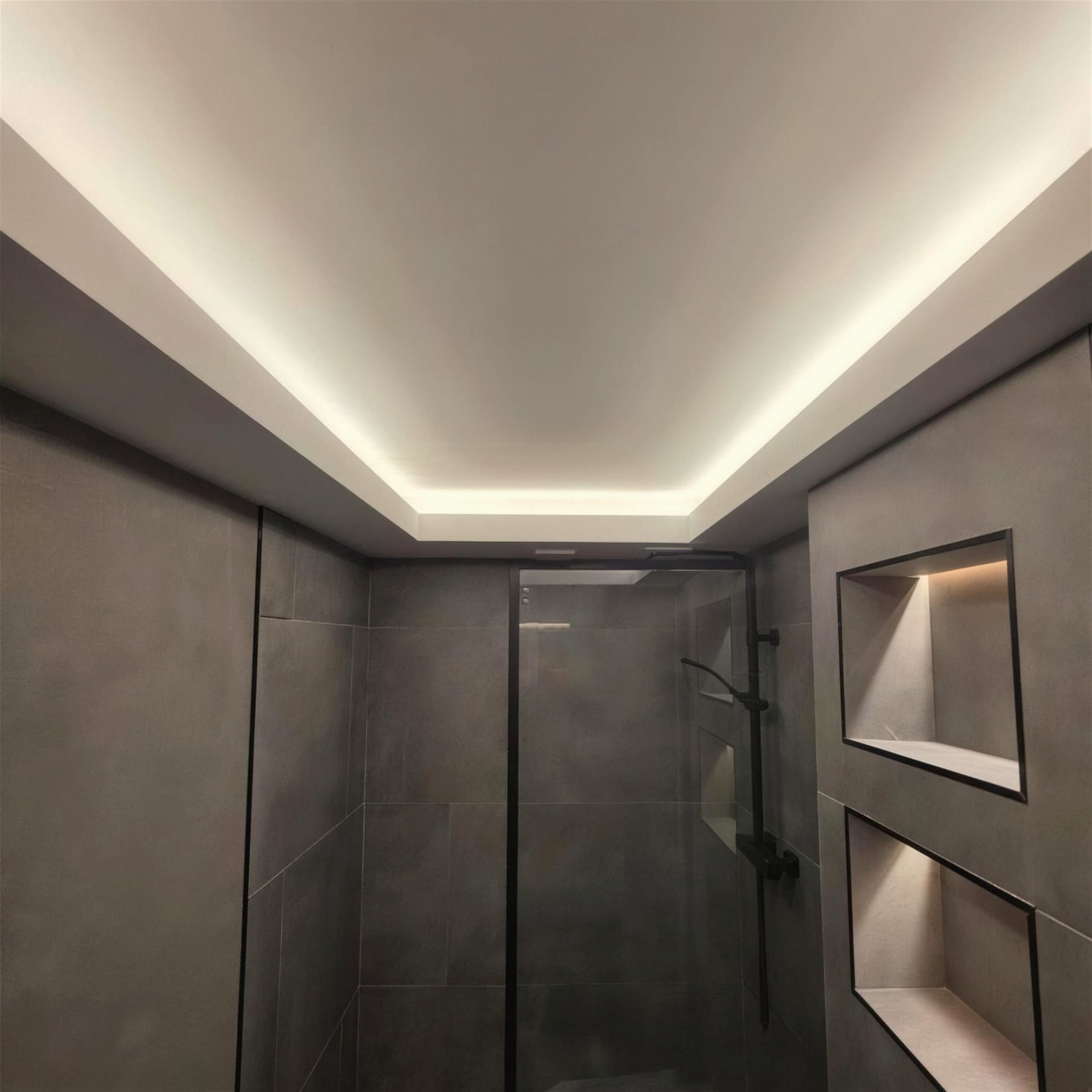 Bathroom ceiling with a continuous warm LED cove above a dark grey shower enclosure with lit storage niches.