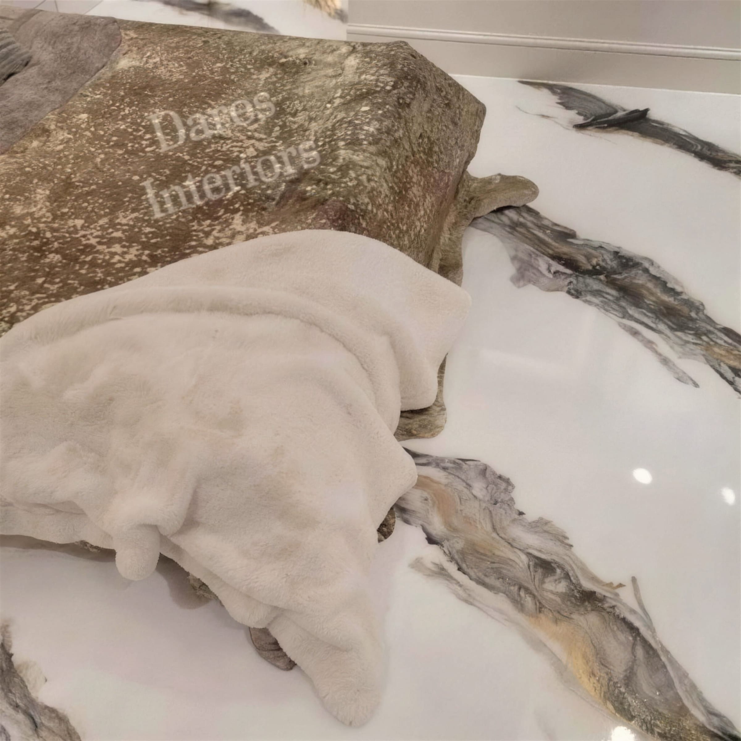 Detail of a glossy white metallic floor with bronze and charcoal veining, styled with a cream faux-fur throw and gold-flecked seat.