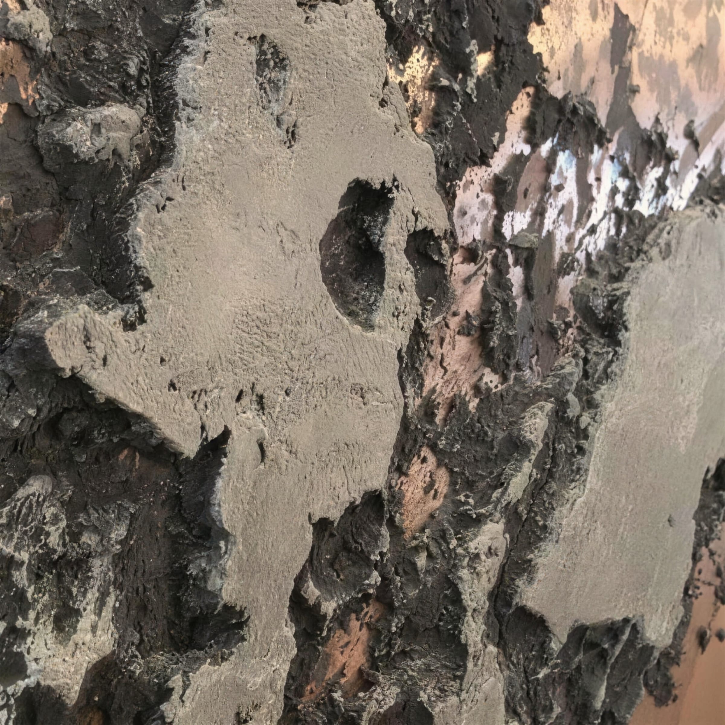 Macro detail of charcoal volcanic texture breaking over gleaming copper metallic plaster beneath.