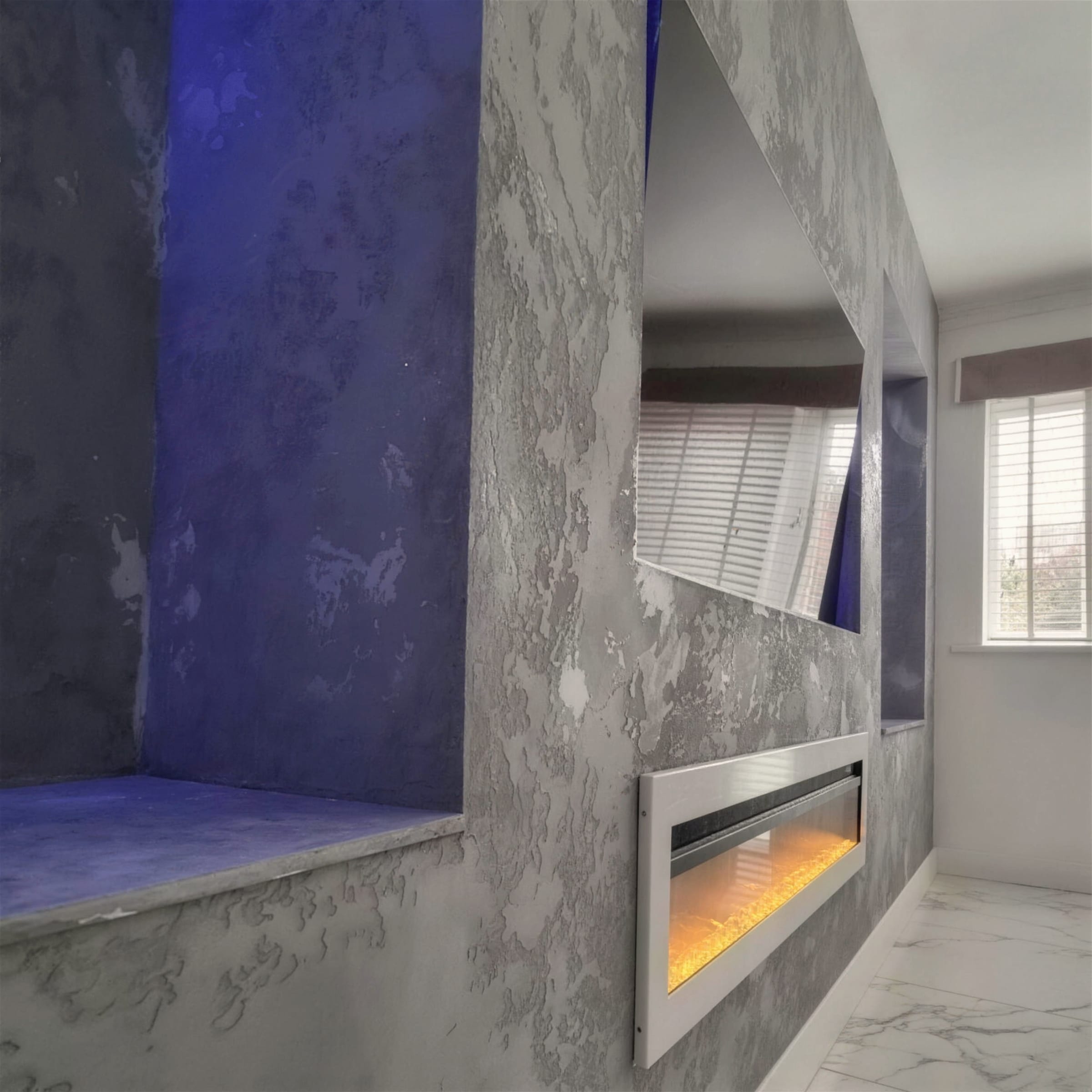 Heavily distressed silver metallic plaster fireplace wall, blue LED niche seat and amber-lit inset fire on marble-effect floor.