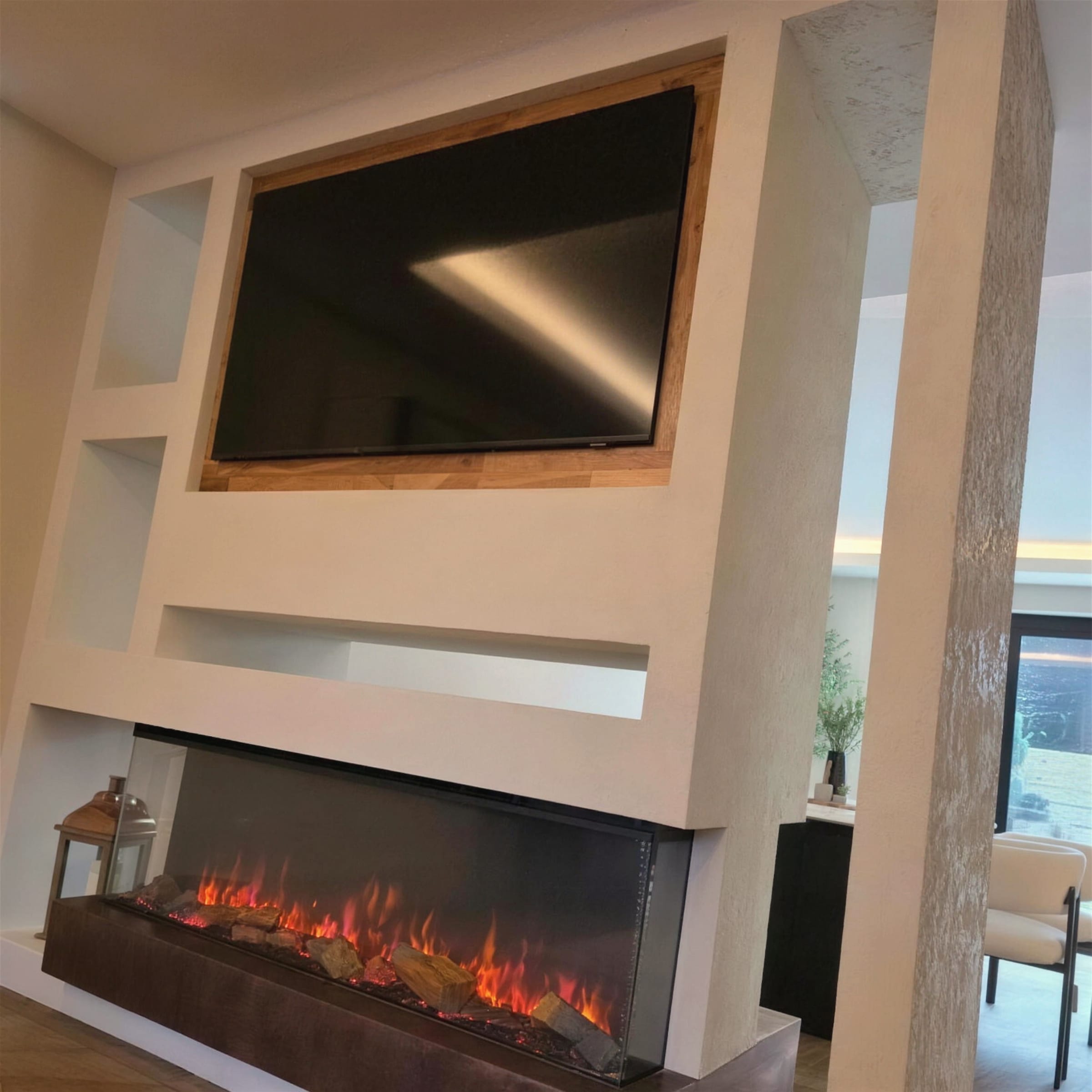 Cream heavily-textured marmorino media wall framing a recessed TV and a lit three-sided linear fireplace on a bronze hearth, shot close and angled upward with daylight from a rear window.